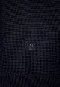 Marinblauer Strickpullover mit einem strukturierten Muster und einem kleinen quadratischen Logoetikett mit dem Buchstaben "M", der in die Ecke gestickt ist.