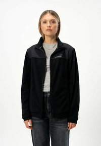 Černá fleecová bunda s vysokým límcem a zapínáním na zip, vyznačující se kontrastními černými ramenními panely a měkkou texturou.