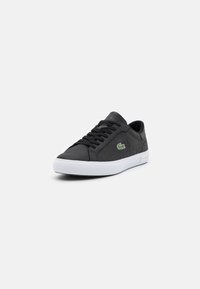 Baskets en cuir noir avec un design texturé, semelle en caoutchouc blanc et lacets noirs. Présente un logo Lacoste vert brodé sur le côté.