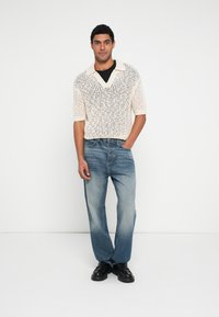 Suéter de punto crema de manga corta con cuello en V, combinado con jeans azul claro y zapatos negros. Textura suave, ajuste relajado.