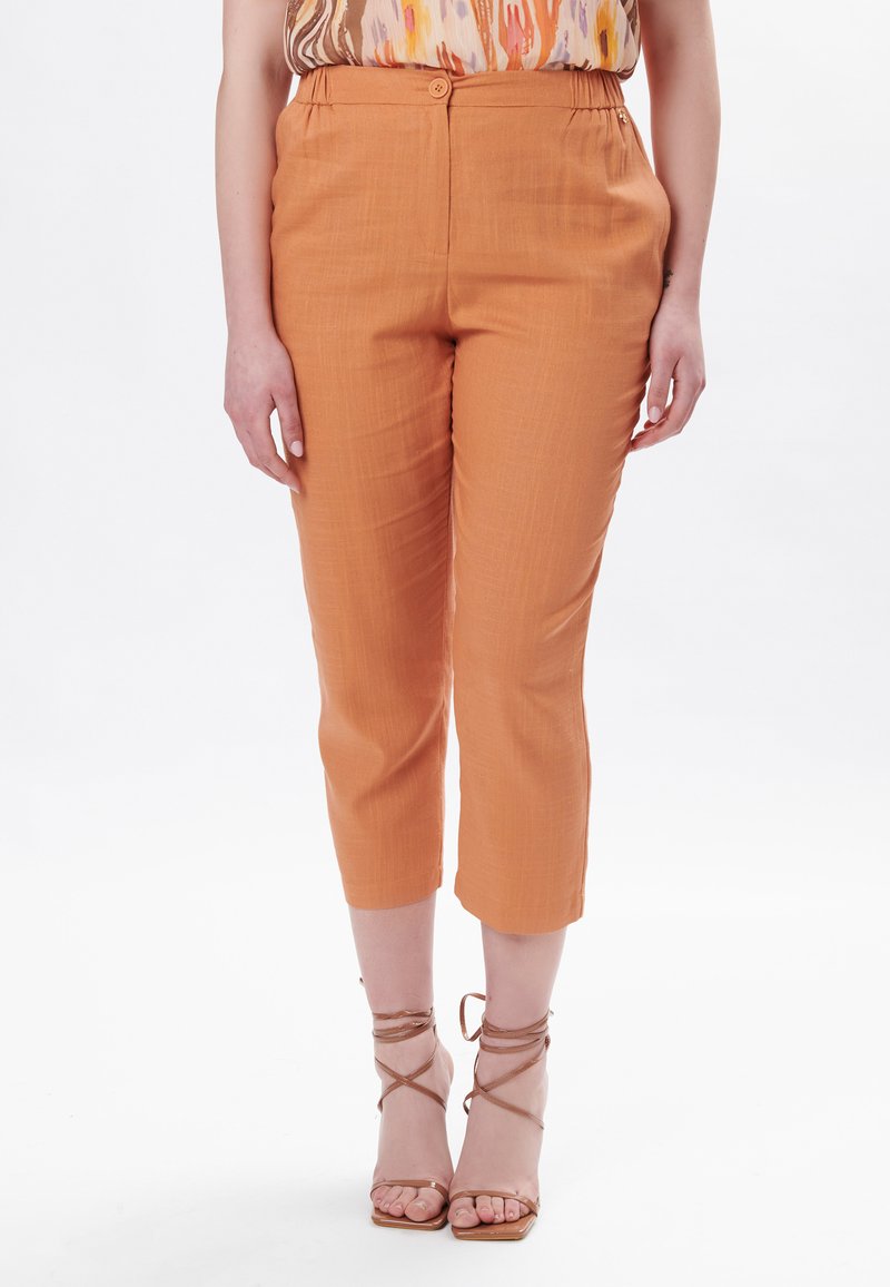 Orange cropped bukser med en glat tekstur, der har en knaplukning og elastisk talje. Kombineret med strop sandaler i nude.