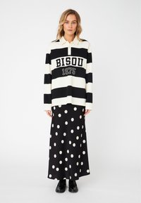 Black and white striped long-sleeve polo shirt with "BISOU 1975" text, paired with a black polka dot maxi skirt. Smooth fabric, relaxed fit.