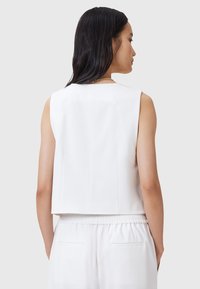 Weißes ärmelloses Cropped Top mit geradem Schnitt, das über eine subtile Textur und klare Linien verfügt. Der Rücken hat einen verdeckten Reißverschluss und Plissee-Details.