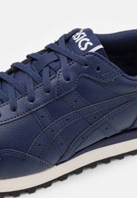 Zapatilla de cuero azul marino con acentos de textil, que cuenta con una suela resistente, costuras prominentes y detalles perforados en los laterales.