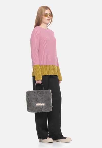 Maglione rosa a coste con un orlo metallico dorato, pantaloni neri a gamba larga e una borsa grigia e pelosa con un logo. Il modello indossa occhiali con lenti gialle.