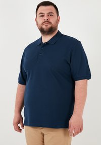 Tamsiai mėlynas polo marškinėliai, pagaminti iš medvilnės, su smailiu apykakle, trimis mygtukais ir trumpomis rankovėmis. Lygus paviršius.