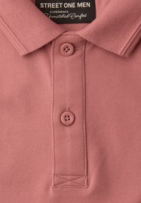 Herre polo i støvet lyserød med krave og to knapper samt sort mærkat med teksten "Street One Men, Oplev uovertruffen komfort."