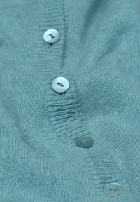 Cardigan en tricot bleu clair avec une surface texturée ; se ferme par trois boutons de couleur claire sur le devant. Tissu doux et confortable.