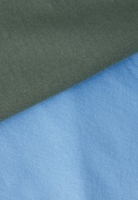 Δύο κομμάτια ριμπ ύφασμα, ένα ελιάς που επικαλύπτει ένα γαλάζιο, και τα δύο σε κοντινή λήψη με ορατή υφή.