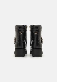 Botas de tobillo de cuero negro con un acabado suave, con acentos de corazón dorados en el costado, cierre de cremallera y resistentes tacones en bloque.