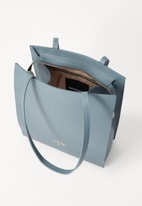 Blue leather tote bag with smooth texture, two handles, gold logo detail, open top, and a zipper pocket inside for secure storage.