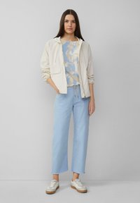Chaqueta ligera de crema con capucha, top azul con estampado de azaleas, pantalones cortos de color azul claro y zapatillas beige con acentos en blanco.