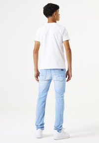 Vaqueros de mezclilla azul claro con un corte ajustado, que cuentan con un diseño de cuatro bolsillos y costuras sutiles. Combinados con una camiseta blanca lisa y zapatillas blancas.