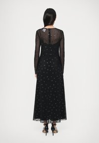 Čierne dlhé šaty s bodkovaným vzorom, priesvitnými dlhými rukávmi, priliehavým živôtikom a voľnou sukňou; majú skrytý zips na chrbte.