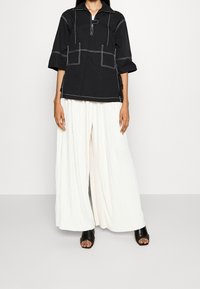 Svart bomullstopp med vit kontrastsöm, trekvartslånga ärmar och uttagen krage, i kombination med vita plisserade vida byxor.