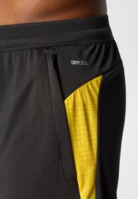 Sorte atletiske shorts i tekstureret stof, med et gult mønstret sidepanel og et synligt "DRYCELL" label på taljen.