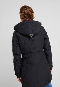 Abrigo acolchado negro con capucha, que presenta un detalle de cintura ajustada en la parte posterior, mangas largas y un diseño de longitud media. La tela parece texturizada y aislante.