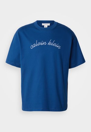T-shirt en coton bleu avec un col rond et des manches courtes, portant "calvin klein" élégamment brodé en cursif blanc sur la poitrine.