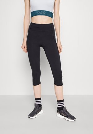 Leggings capri noirs avec taille haute et coutures latérales. Associés à un haut court gris et des chaussures de sport noires avec des accents blancs.