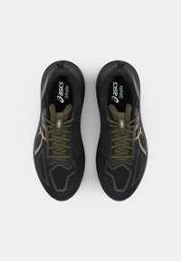 Black athletic shoes with a textured upper, featuring olive green laces and accents. "GORE-TEX" branding on the side and cushioning insole visible.