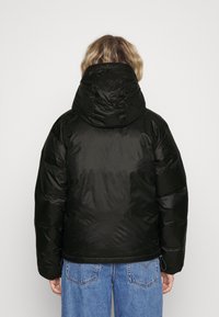Sort dunjakke med hætte, med en glat og skinnende overflade. Ribbet detaljer og en cropped pasform. Bæret med lyseblå jeans.