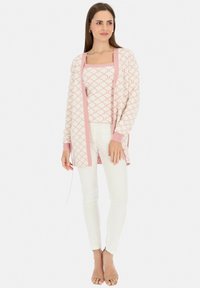 Lekki, wzorzysty kardigan w różowo-białe paski, z otwartym przodem, zestawiony z topem o kwadratowym dekolcie i białymi dopasowanymi dżinsami. Całość dopełniają sandały.