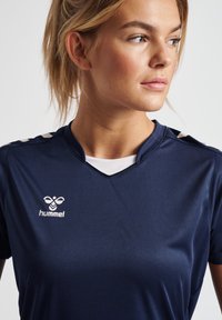 Navy sports jersey med korte ærmer, v-hals design. Har en hvid accentstribe på skuldrene og et Hummel-logo på fronten.
