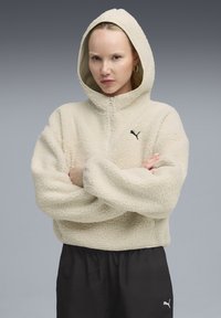 Beiger Fleece-Pullover mit Kapuze, Reißverschluss und Logo. Aus dicken, strukturierten Stoff gefertigt und mit lockeren Ärmeln für mehr Komfort.