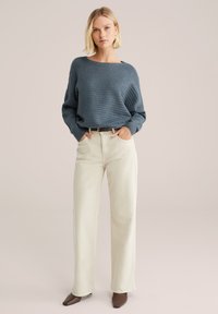 Blauer gerippter Pullover mit weitem Ausschnitt, kombiniert mit cremefarbenen gerade geschnittenen Hosen. Braune spitze Absatzschuhe runden das Outfit ab.