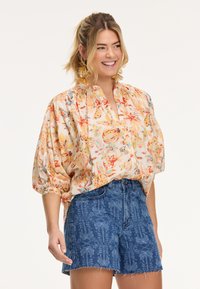 Blouse à imprimé floral en tissu doux avec des manches bouffantes et un col mandarin, associée à un short en denim taille haute avec un motif.