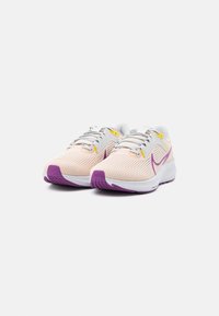 Zapatillas de correr ligeras con una parte superior de malla suave en rosa claro, entresuela blanca y acentos morados en la suela y el logotipo lateral. Diseño con cordones.