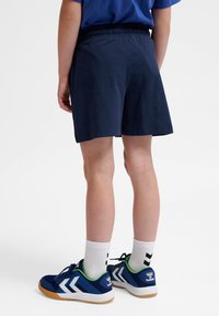 Mörkblå bomullsshorts med elastisk midja, ihop med blå skor med vita zick-zack detaljer och vita strumpor.