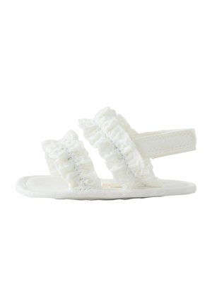 White baby sandal with two ruffled fabric straps and a back strap, flat sole, and soft textured material.