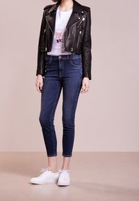 Musta nahkamoottoripyörätakki, valkoinen graafinen t-paita, tummansiniset skinny-farkut ja valkoiset lenkkarit, joissa on vetoketjuja ja kissakuva.