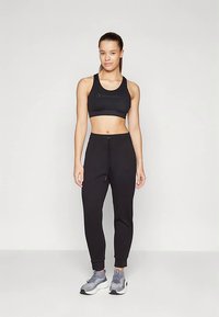 Zwarte sportbeha en joggingbroek met een trekkoord in de taille. Gestructureerde stof, gecombineerd met grijze sportschoenen. Eenvoudig en functioneel ontwerp.