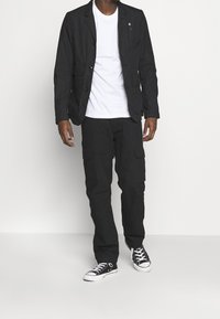 Svart lätt blazers med en enda ficka och knappar, i kombination med cargobyxor, avslutad med svart och vita sneakers. Enkel vit T-shirt underneath.