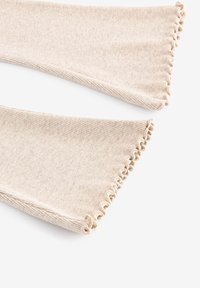 Tela de punto beige con textura acanalada, que presenta un diseño acampanado y un borde fruncido. Tonos suaves y sutiles que complementan diversos conjuntos.