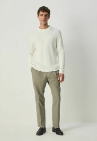 White knitted sweater with a round neckline, paired with light grey trousers and black shoes, creating a textured and layered look.