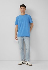 Koninklijk blauwe T-shirt met korte mouwen, ronde hals, gecombineerd met lichtblauwe denim jeans en witte sneakers met zwarte accenten. Glad textuur.