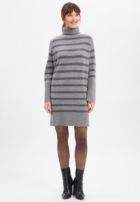 Szara sukienka w paski z golfem i długimi rękawami, wykonana z miękkiego materiału. Posiada ciemniejsze szare paski, prążkowany dół, noszona z czarnymi botkami za kostkę.