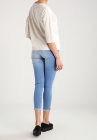 Svetle béžová, tečkovaná halenka s tříčtvrtečními rukávy v kombinaci s úzkými, světle modrými džíny s ohrnutými rukávy a černými klouzavými botami.