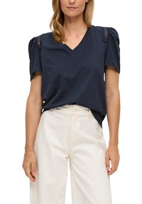 Navyblauwe V-hals T-shirt met korte pofmouwen, voorzien van kantdetails op de schouders, in combinatie met lichtgekleurde wijde broekspijpen.