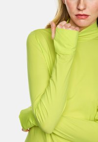 Long-sleeved, lime green top made of stretchy material with a high neckline and thumbholes at the cuffs for enhanced comfort and coverage.