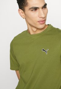 Olivengrøn bomulds T-shirt med rund halsudskæring. Har et lille sort og hvidt broderet logo på venstre bryst. Korte ærmer.