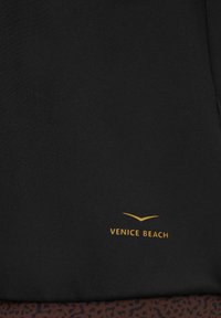 Schwarzes Sportstoff-Oberteil mit einem goldenen "VENICE BEACH"-Logo. Das Design zeichnet sich durch eine glatte Textur und einen leichten Glanz aus.