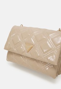 Beige prošívaná taška z lakované kůže s zlatým trojúhelníkovým logem, s klopou a řetízkem. Design zahrnuje vzory ve tvaru diamantů.