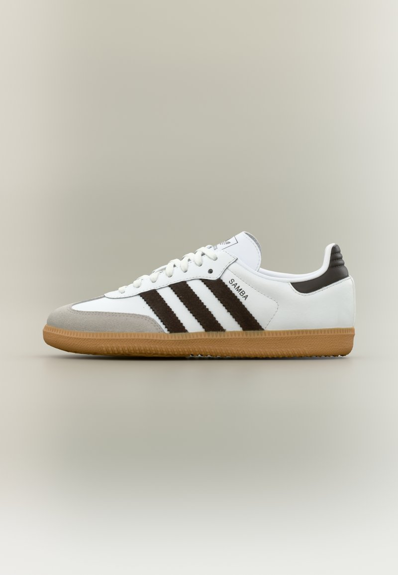 White sneaker with brown stripes and gray suede toe cap. Features a gum rubber sole and textured detailing on heel. Brand label visible.