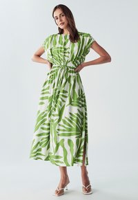 Zelena i bijela prugasta haljina opuštenog kroja, s naboranim strukom i kratkim rukavima; sadrži botanički print lišća i bočne proreze.