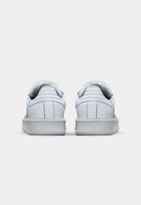 Weiße Sneakers mit Obermaterial aus strukturiertem Leder, gepolstertem Fersenkragen und gerillter Gummisohle. Rückansicht, die das Design und die Nähdetails hervorhebt.