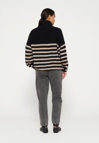 Gebreid trui met een hoge hals, voorzien van marineblauwe en beige horizontale strepen. Gedragen met grijze jeans en zwarte instapschoenen.